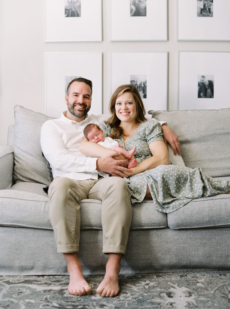 Smiling parents holding newborn baby on a couch