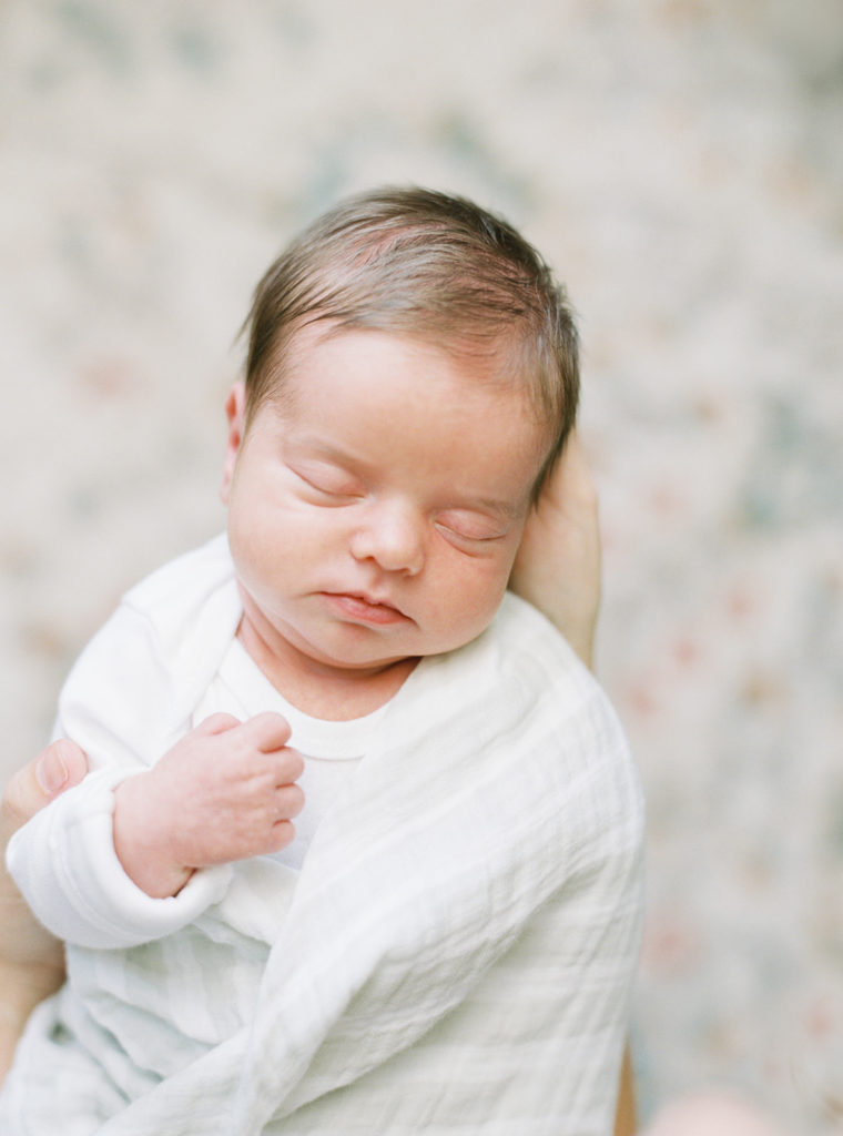 Newborn baby with closed eyes in white swaddle