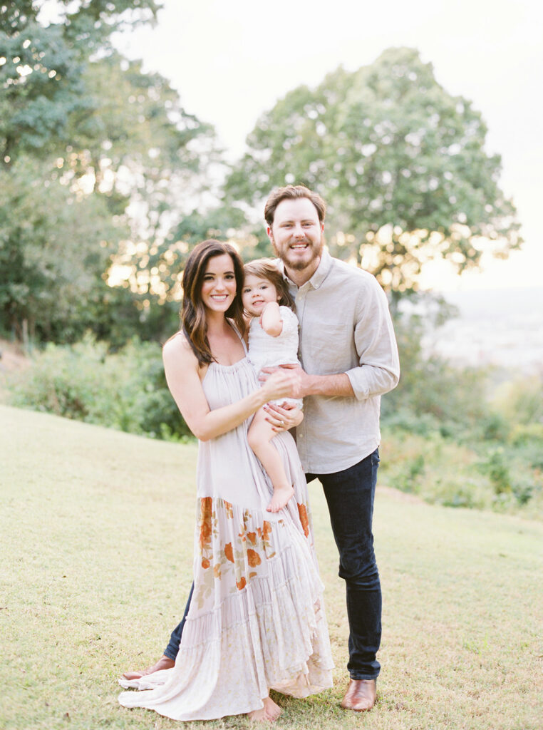 Family of three walking through a Birmingham, AL park in coordinated neutral outfits for timeless fall portraits