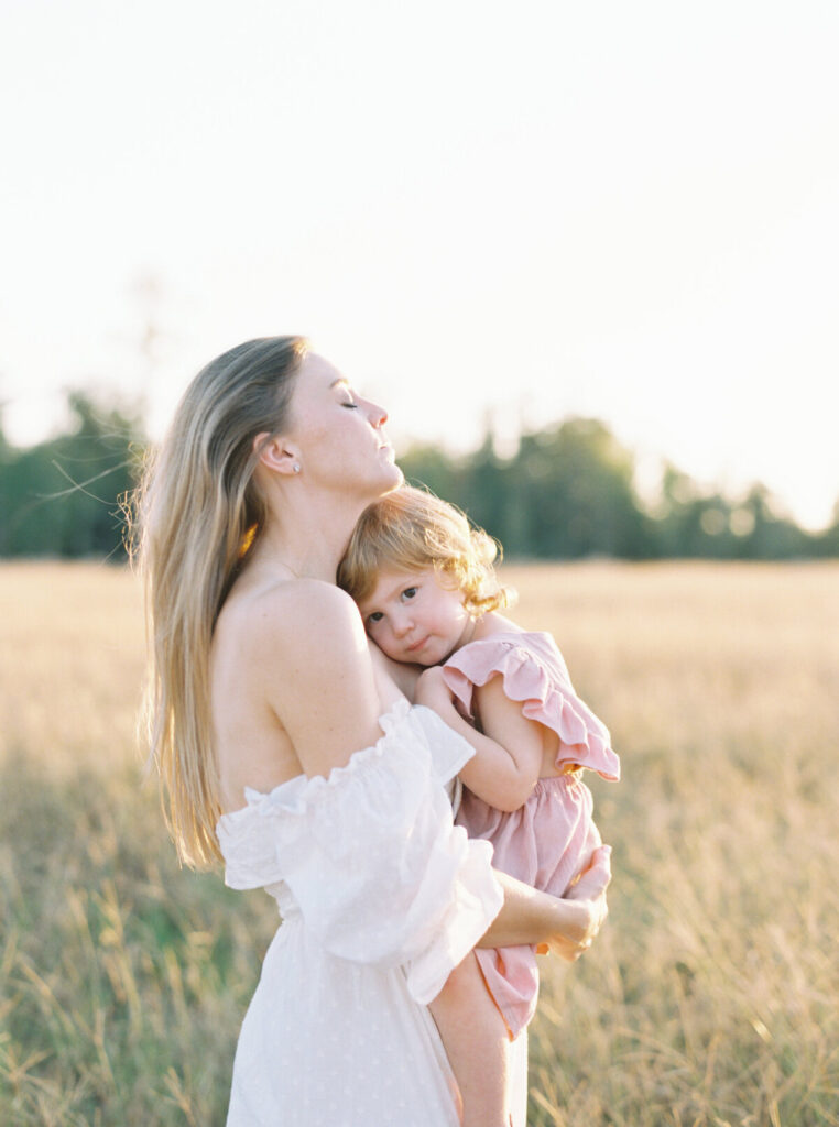 Mom wearing white flowing dress holding daughter in a field during fall family photos