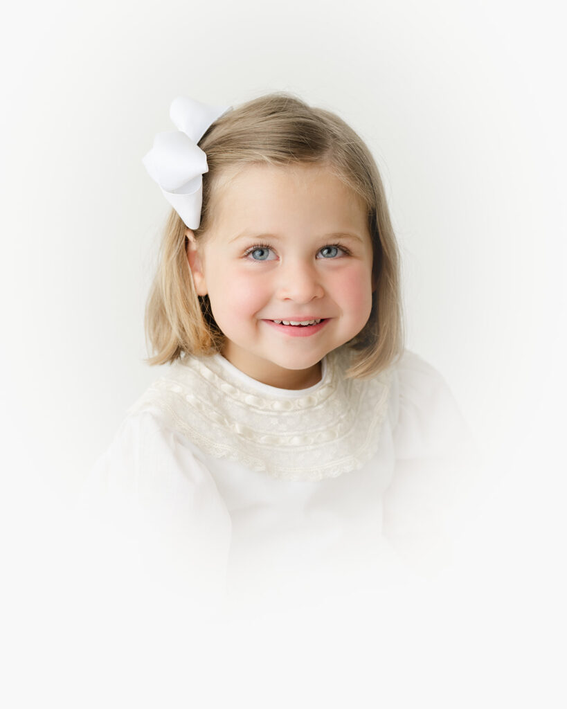 Close-up heirloom portrait showing a child’s gentle smile and bright eyes captured in a classic vignette style.