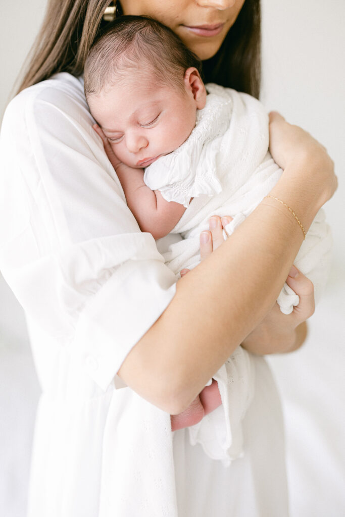 Parent holding their newborn in a classic studio setup, with soft lighting and a clean, timeless aesthetic.
